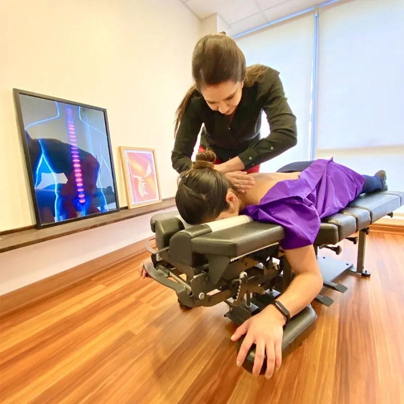 Chiropractor adjusting a patient on the table, next to a spine X-ray on screen