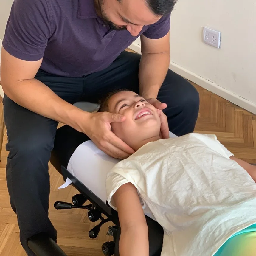 Quiropráctico realizando un ajuste cervical a un niño en la camilla
