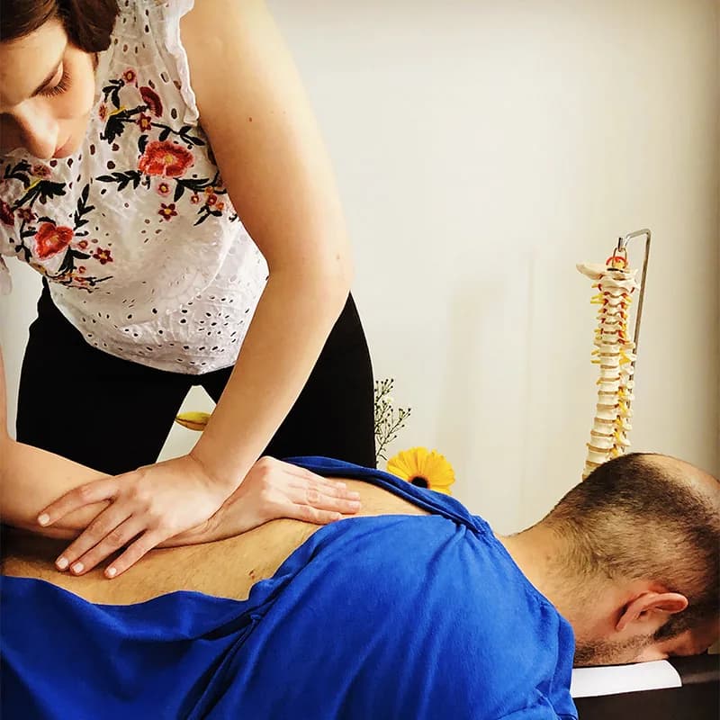Quiropráctica ajustando la espalda de un paciente, con un modelo de columna vertebral al fondo